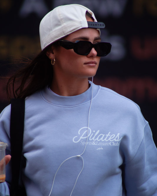 Woman wearing powder blue Pilates Sports & Leisure Club oversized crewneck sweatshirt, streetwear lifestyle photo.